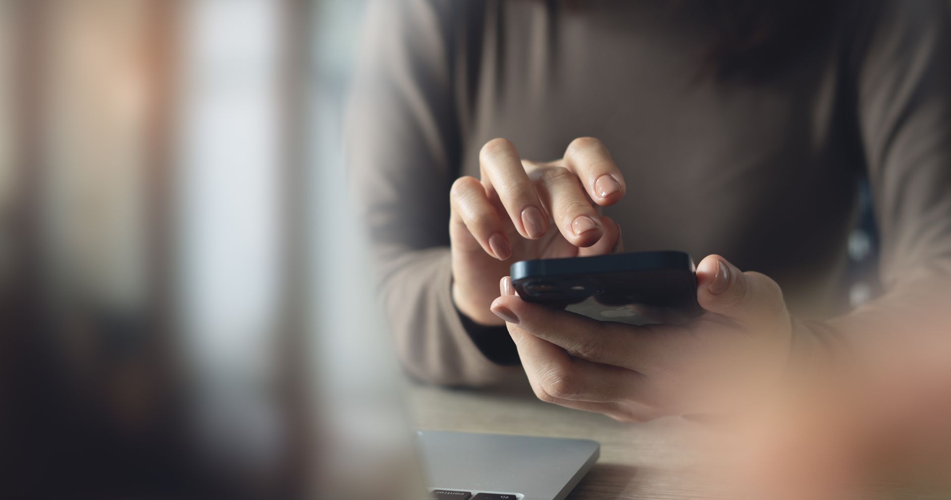 A woman is sitting at a table using a cell phone.