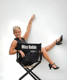 Woman in a director’s chair labeled “Miss Robin,” posing with one arm raised and one leg extended against a white background