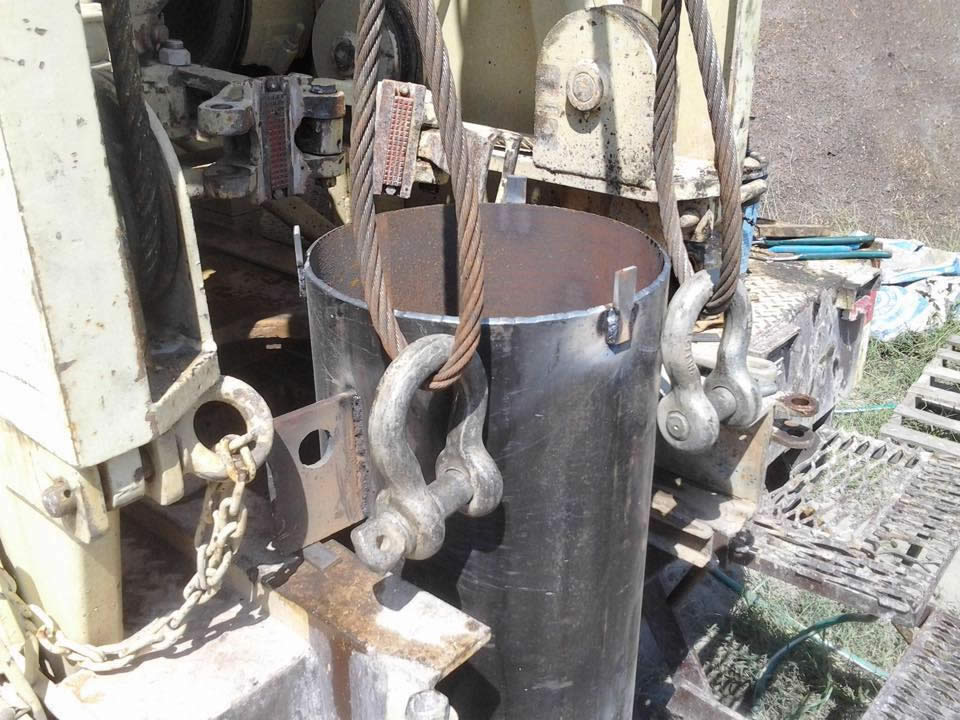 A black metal cylinder being lifted by cables and shackles, likely for construction work.
