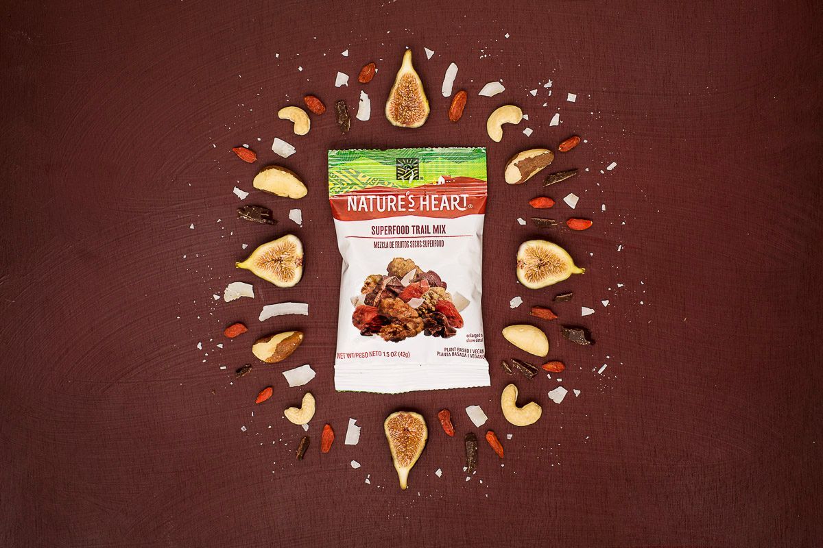 An assortment of dried figs, cashews, goji berries, cacao nibs and coconut flakes on a purple/red background, around Nature's Heart snack mix. Product photography for Nature's Heart by JAM Creative.