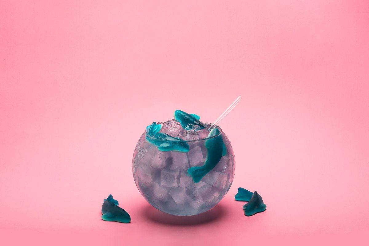 Beverage product photography of blue cocktail with gummy sharks on pink paper. Commercial photography for Stonecutter Spirits