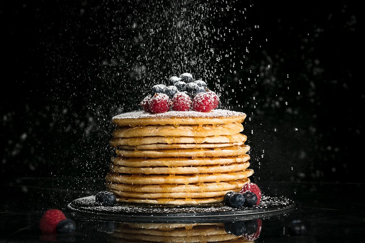 High-end food photography of pancakes, stacked with berries and drizzled with Vermont maple syrup and powdered sugar. Product photography for Runamok Maple by JAM Creative.