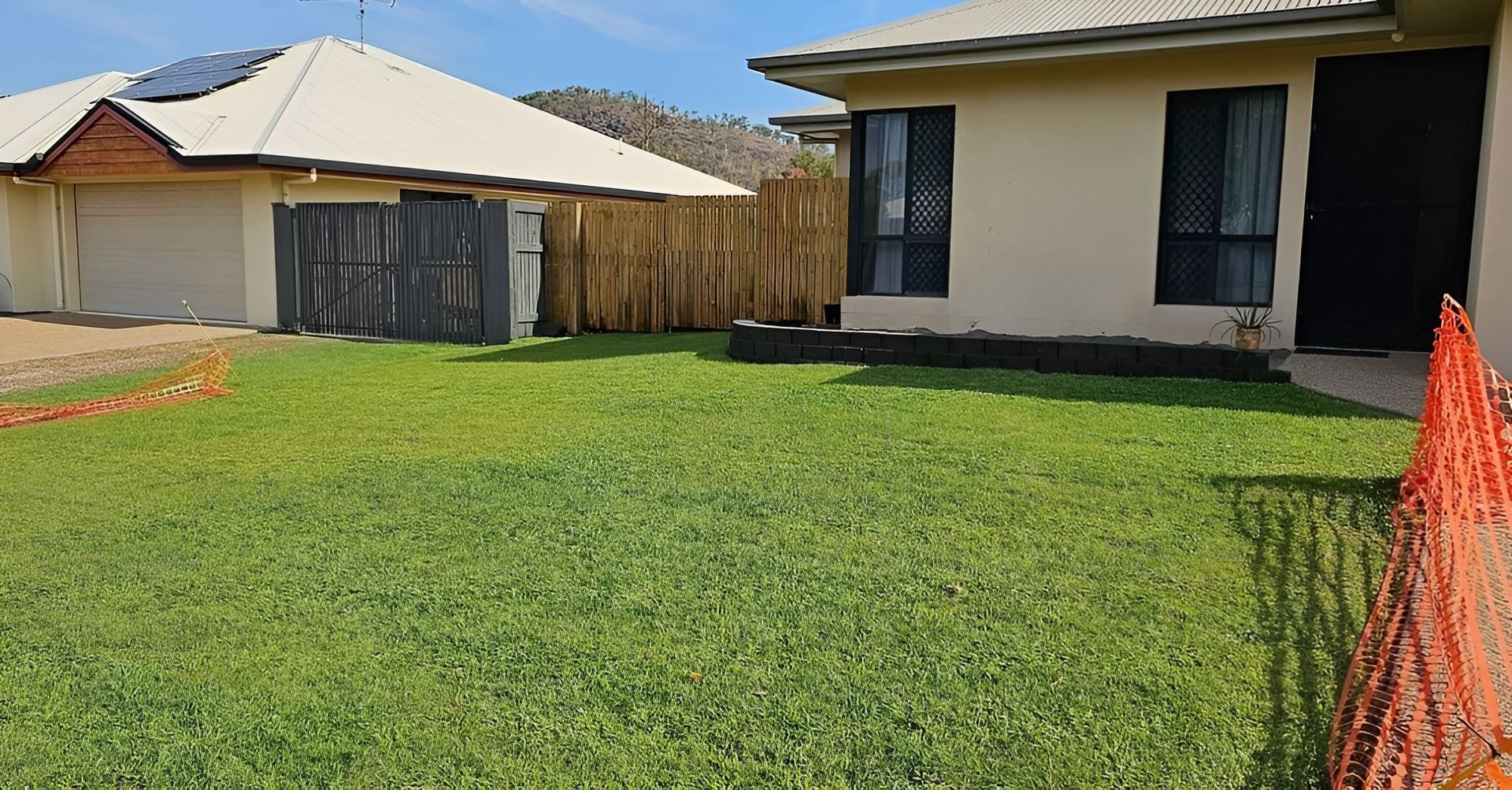 Lawn in Front of A Tan House and Garage with A Wooden Fence — Top Notch Turf in Richmond, QLD