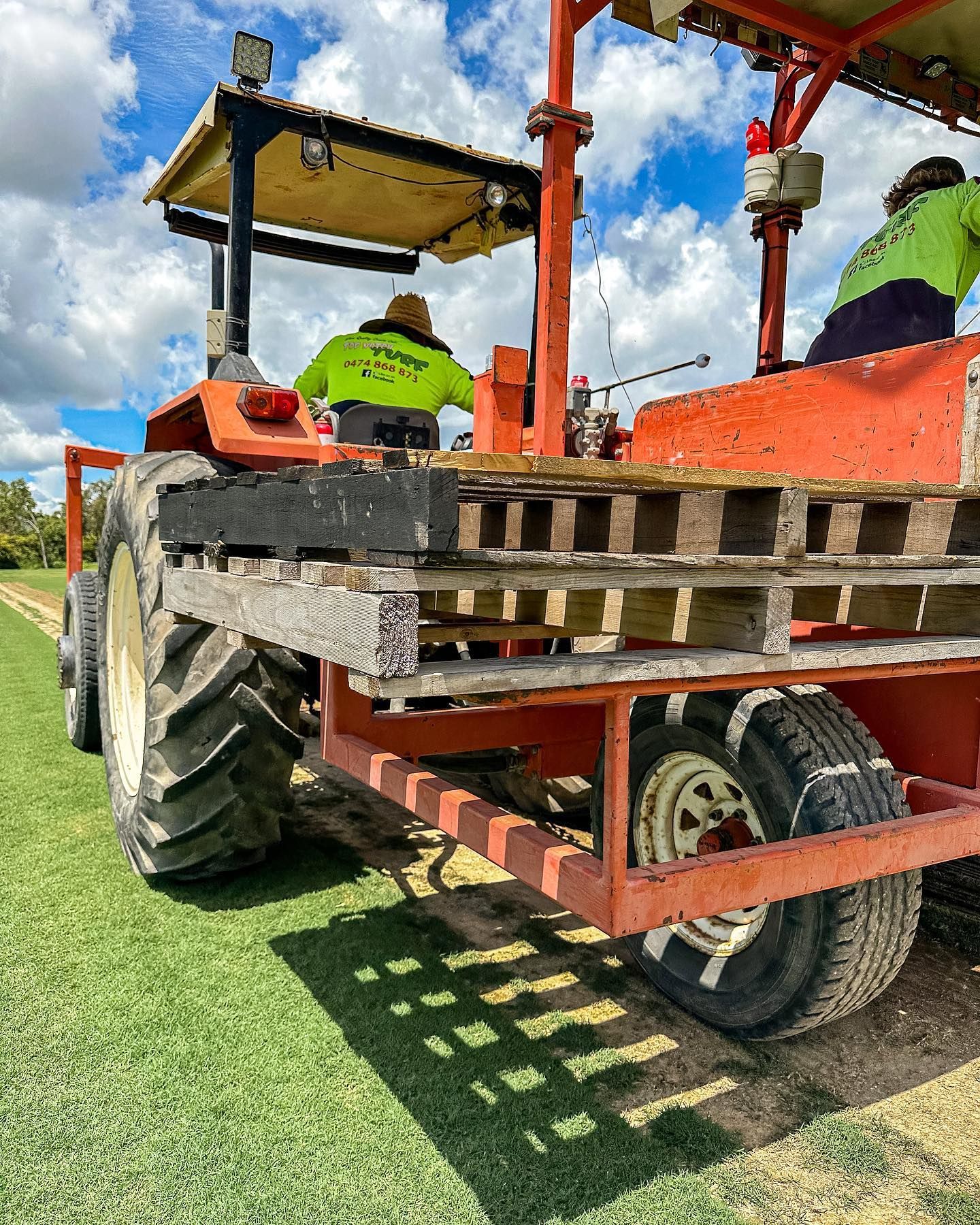 Tractor with Two Workers in Safety Vests on A Grassy Field with A Blue Sky — Top Notch Turf in Rasmussen, QLD