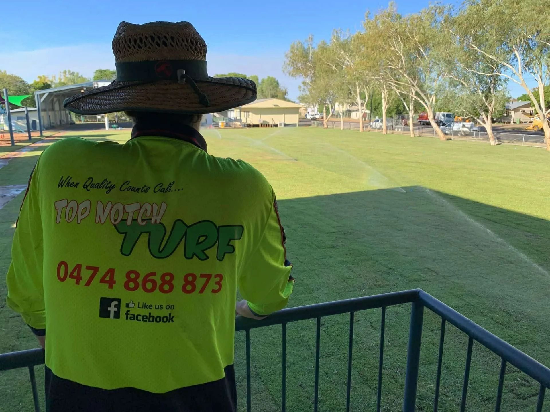 Man in Straw Hat and Neon Shirt Looks out At Irrigated Lawn — Top Notch Turf in Rasmussen, QLD