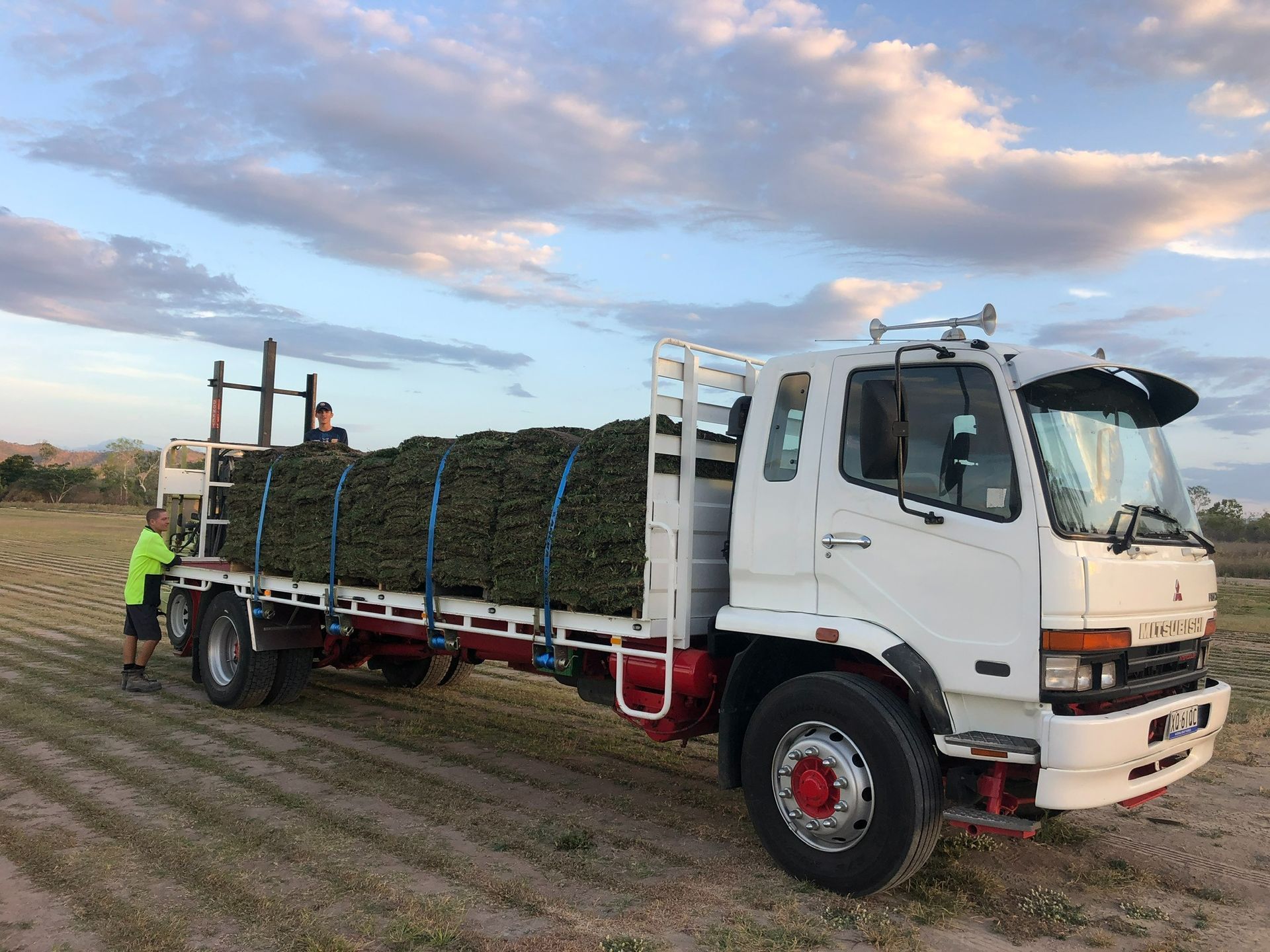 A White Truck Loaded with Green Brush, Two People Standing Near the Truck in A Field — Top Notch Turf in Rasmussen, QLD