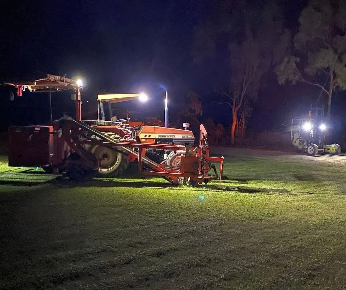 Two Tractors Lit by Bright Lights at Night, One with An Attached Implement — Top Notch Turf in Rasmussen, QLD