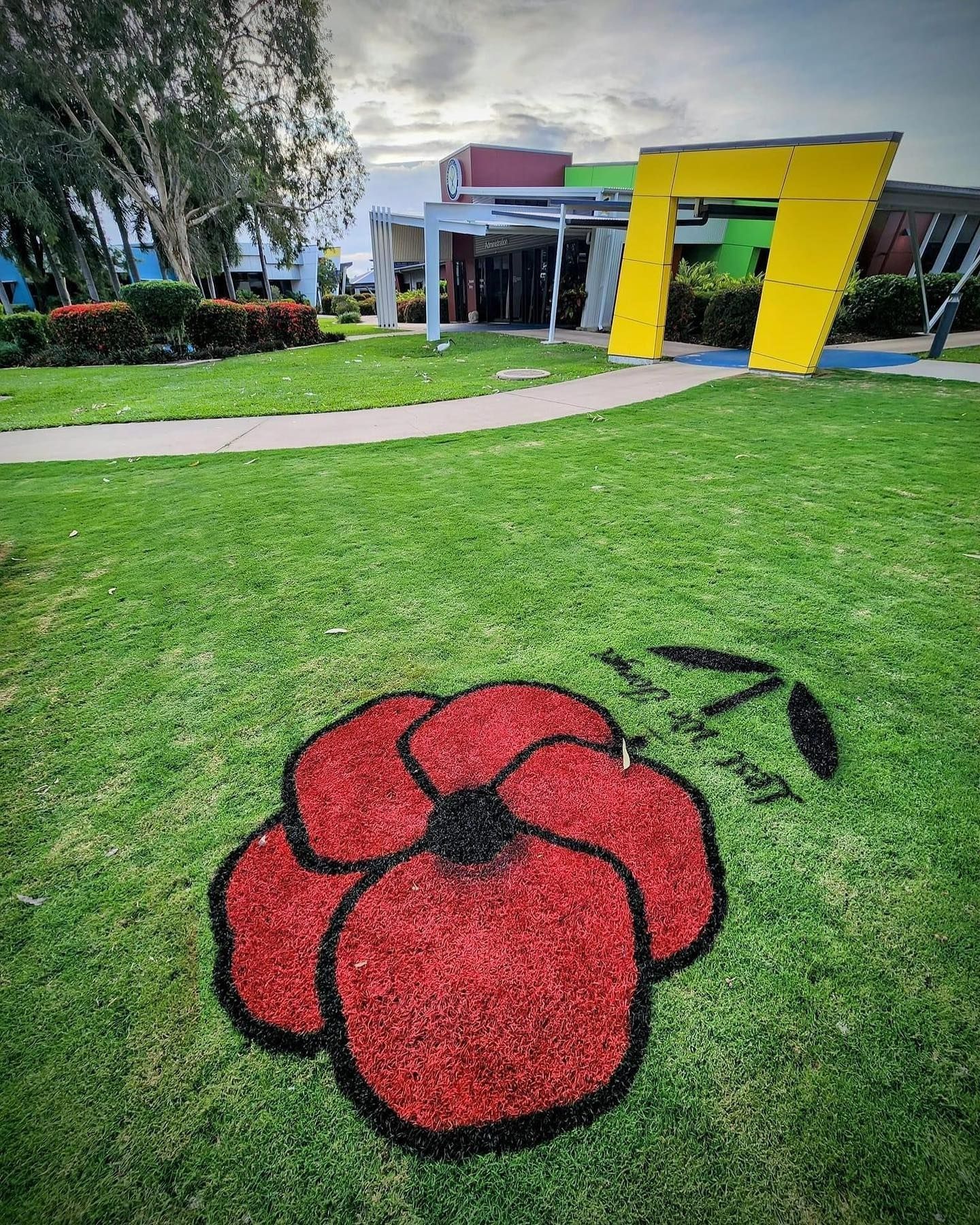Large Red Poppy and Green Leaf Design on Grass, Building and Yellow Sculpture — Top Notch Turf in Rasmussen, QLD