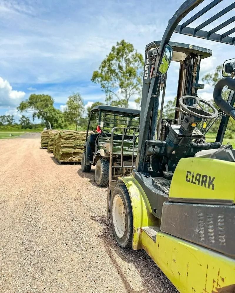 Forklift Towing Utility Vehicle Loaded with Stacked Materials on A Dirt Road — Top Notch Turf in Rasmussen, QLD