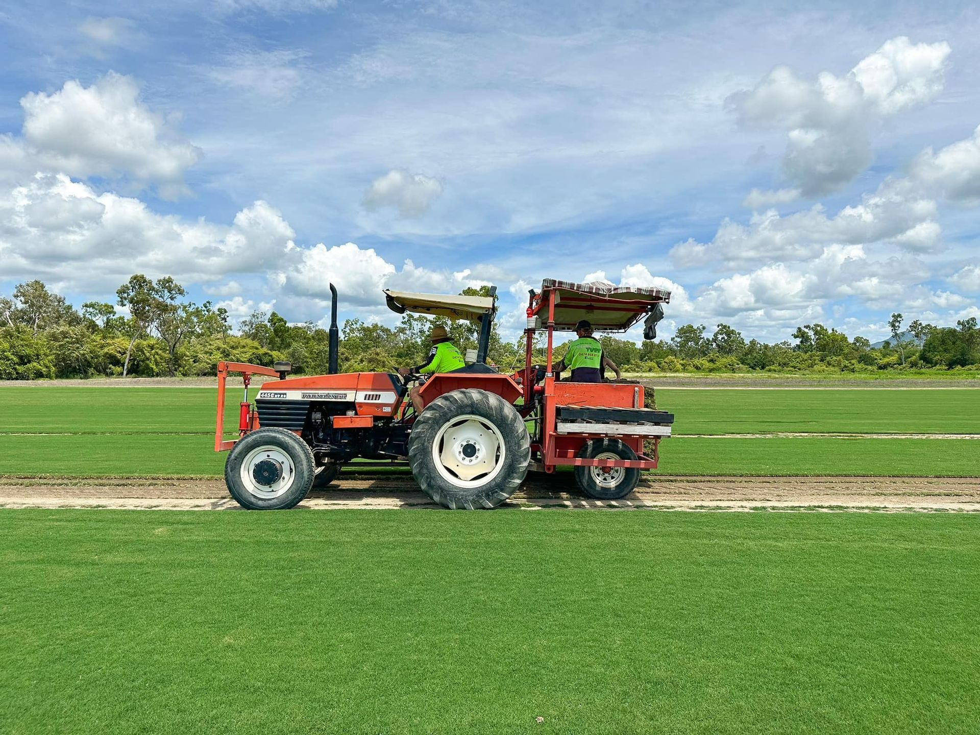 Orange Tractor with Two Workers, Cultivating a Field of Green Plants — Top Notch Turf in Rasmussen, QLD