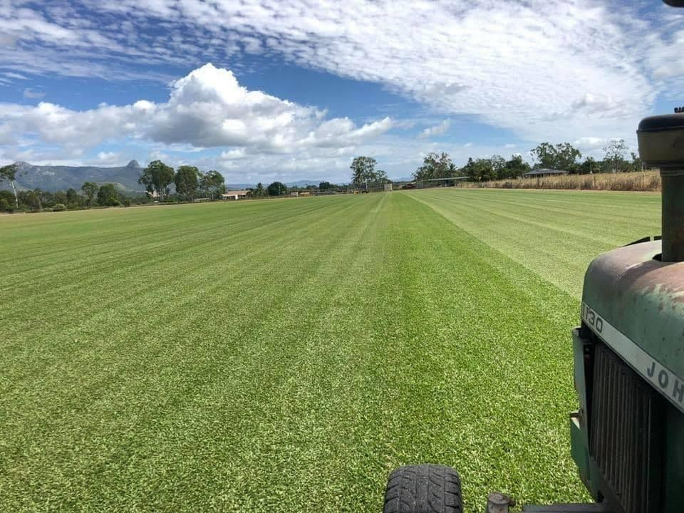 A Tractor Mowing a Large, Green Field with A Mountain Range in The Distance — Top Notch Turf in Rasmussen, QLD