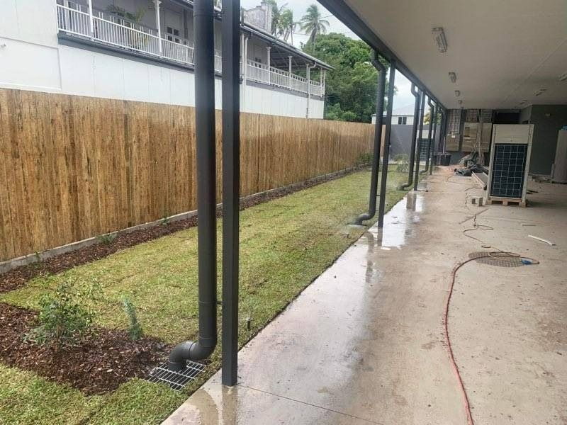 Grassy Area with Bamboo Fence, Dark Downspouts, and Concrete Walkway — Top Notch Turf in Rasmussen, QLD
