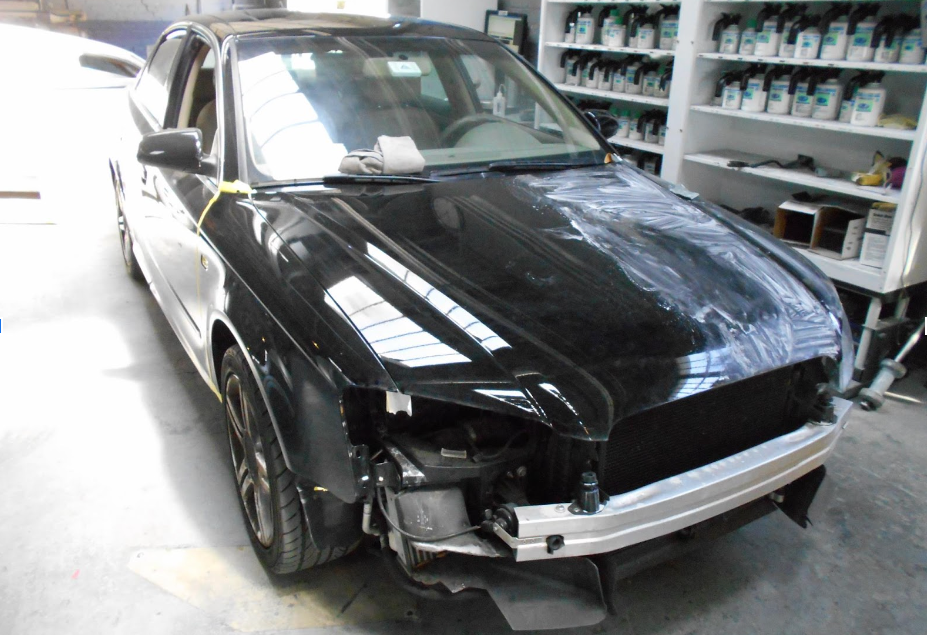 A black car with the hood removed is in a garage