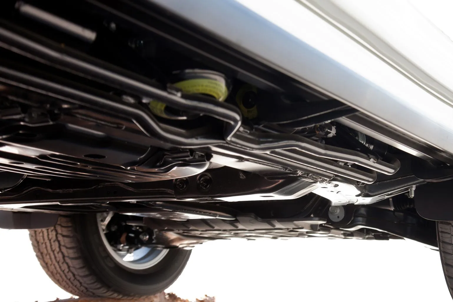 Undercarriage of a vehicle, showing black suspension and exhaust parts with a rear tire visible.