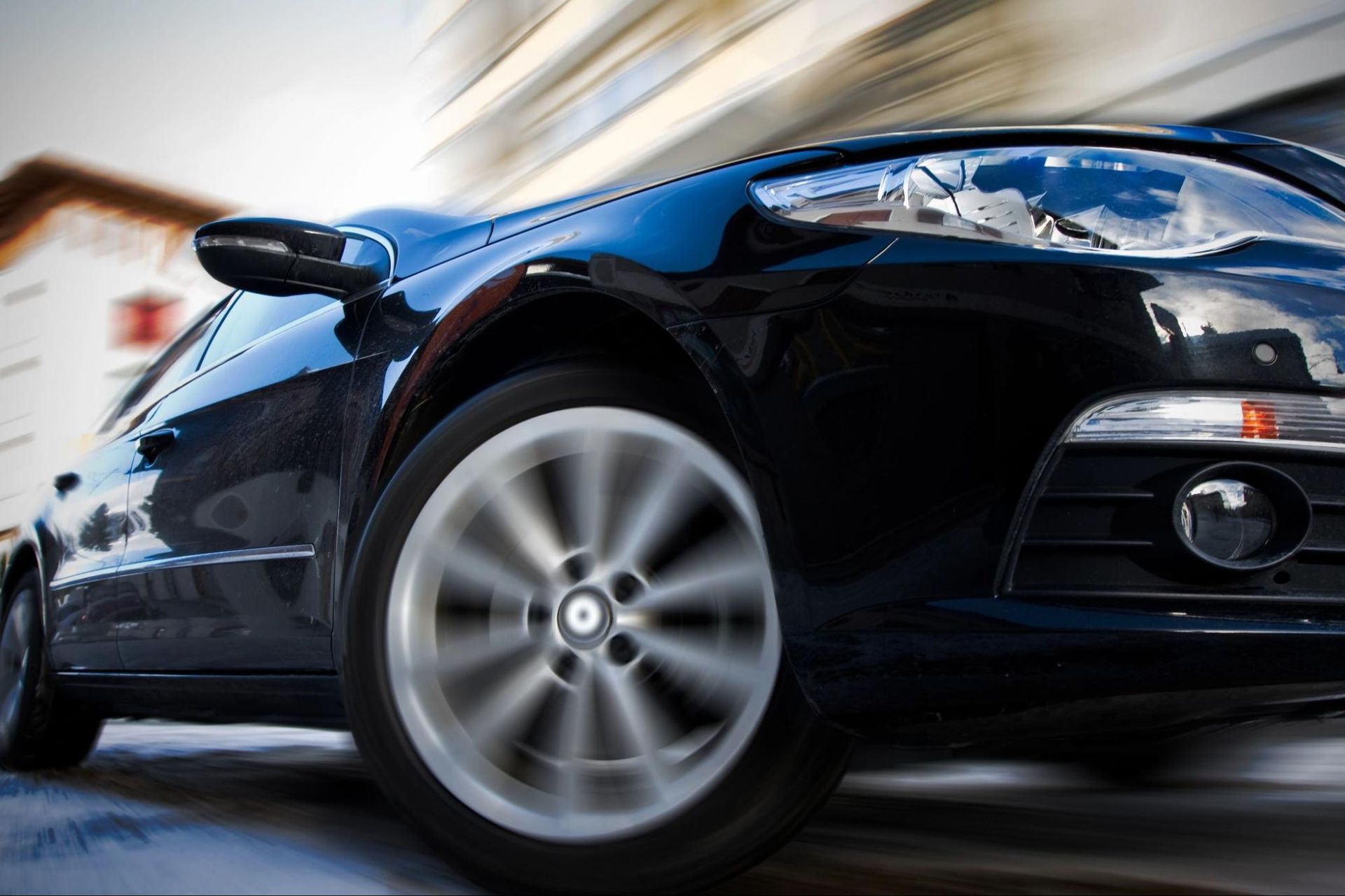 A black car is driving down a street in front of a building.