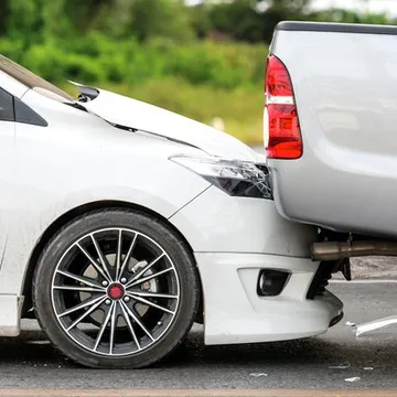 A white car is being towed by a silver truck.