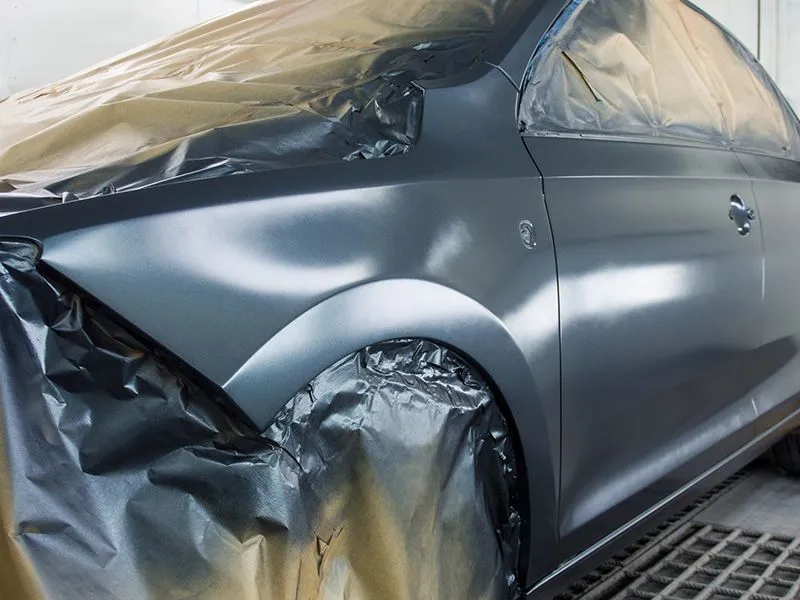 A car is covered in plastic wrap in a paint booth.
