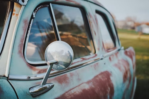 A close up of an old rusty car with a rear view mirror.