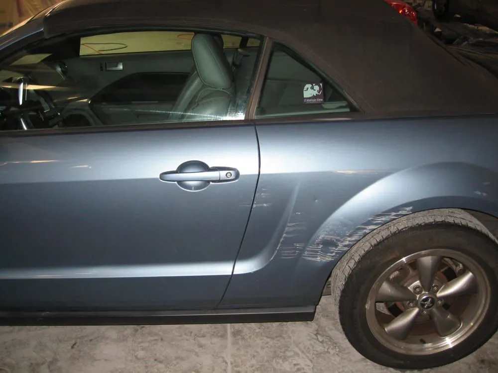 Blue convertible car with significant scratches on the rear quarter panel and door. The top is black.