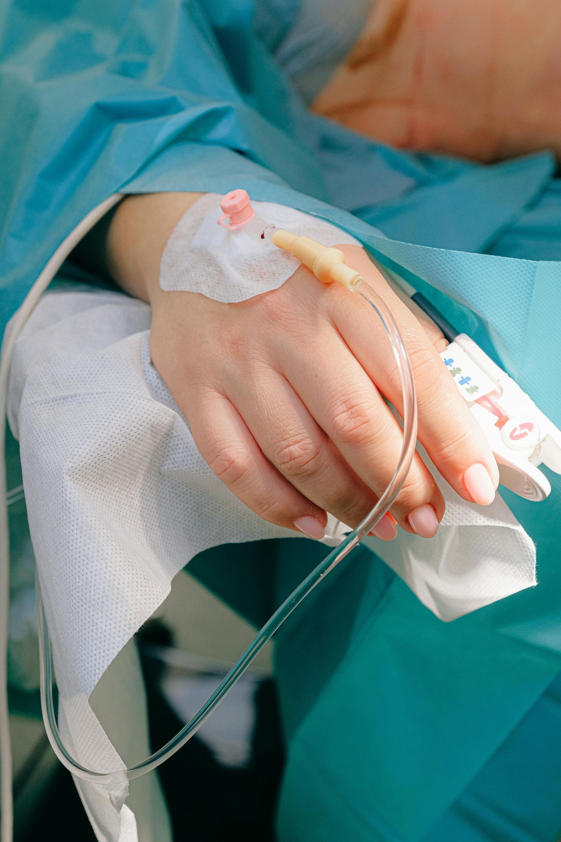 A person is laying in a hospital bed with an iv in their hand.