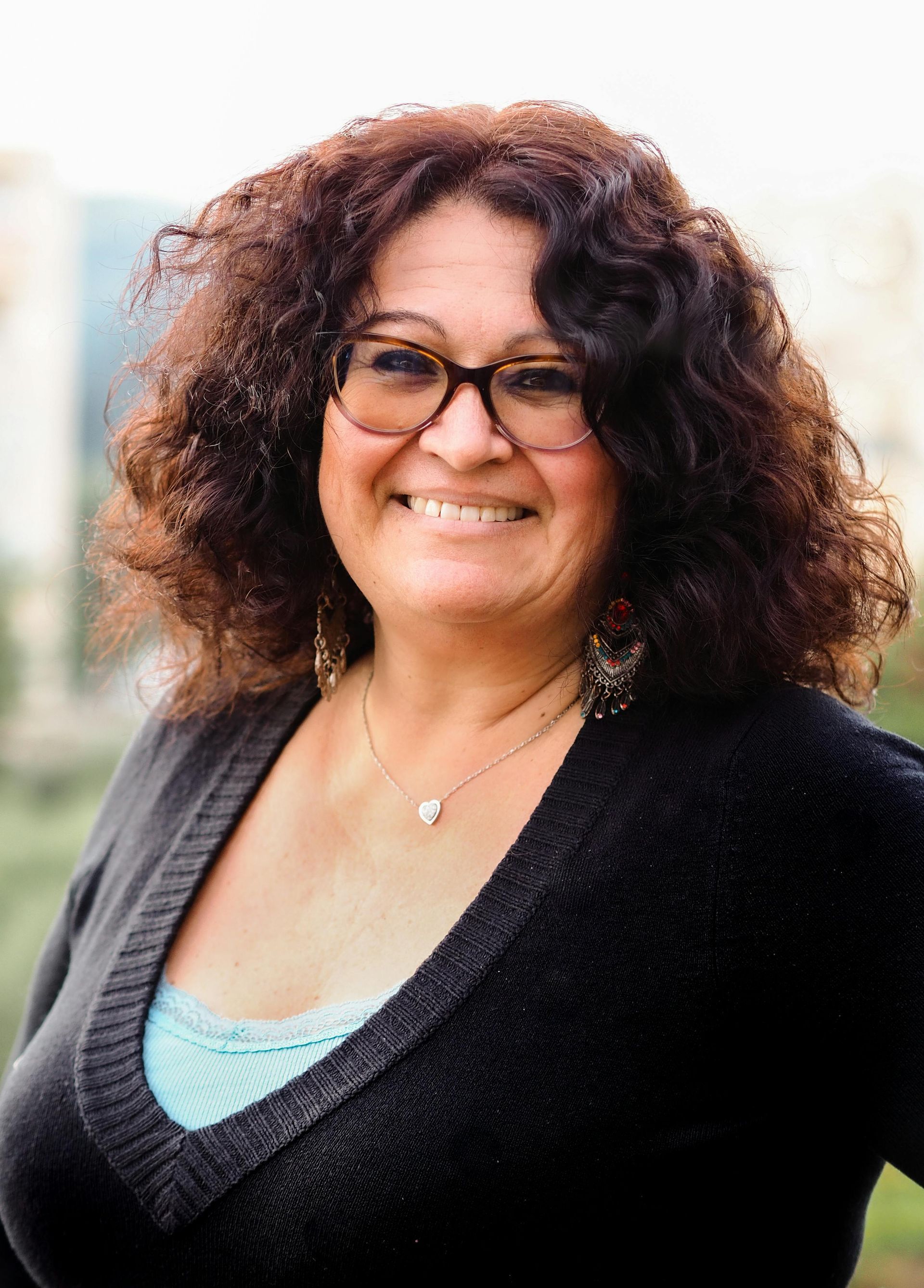 A woman with curly hair and glasses is smiling for the camera.