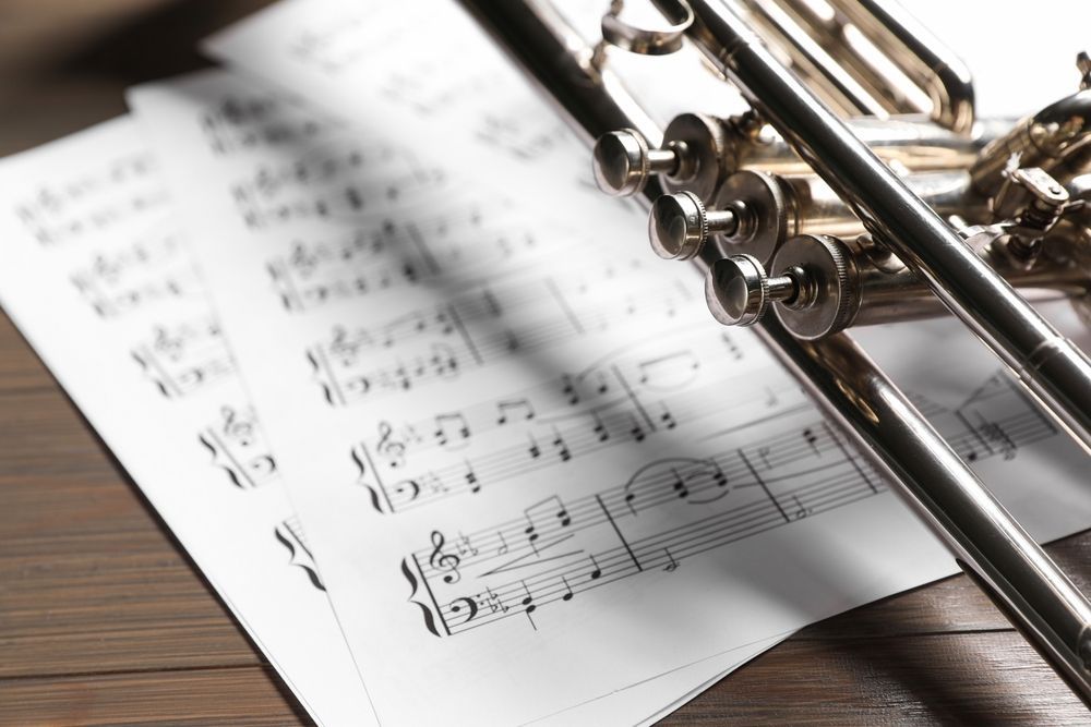 Trumpet on sheet music, resting on a wooden surface.