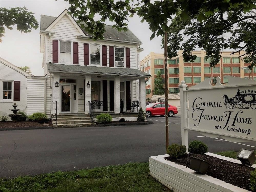 White Colonial Funeral Home with sign; red car parked in front.