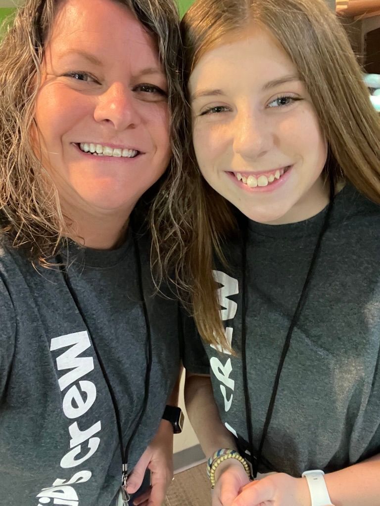 Two smiling people in dark shirts posing closely indoors with sunlight behind them