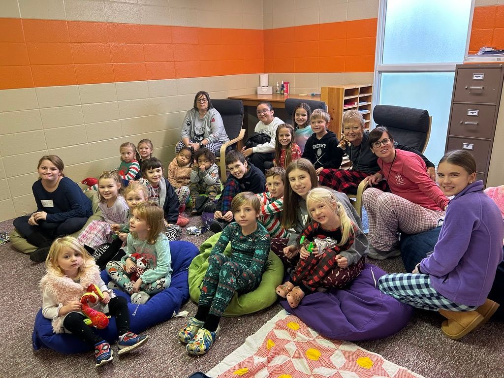 Group of people sitting on the floor in a classroom, smiling and posing together in colorful clothes.