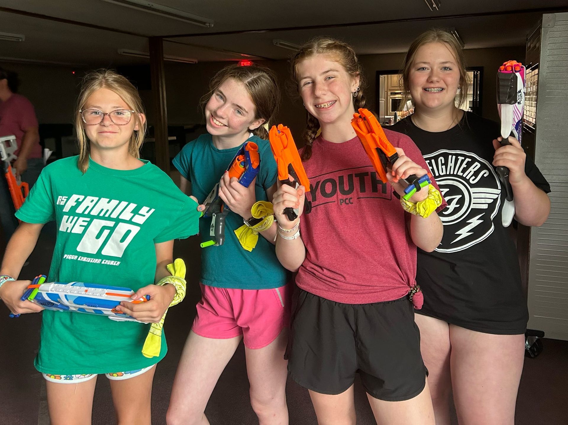 Four teens smiling indoors, holding colorful water guns in a room.