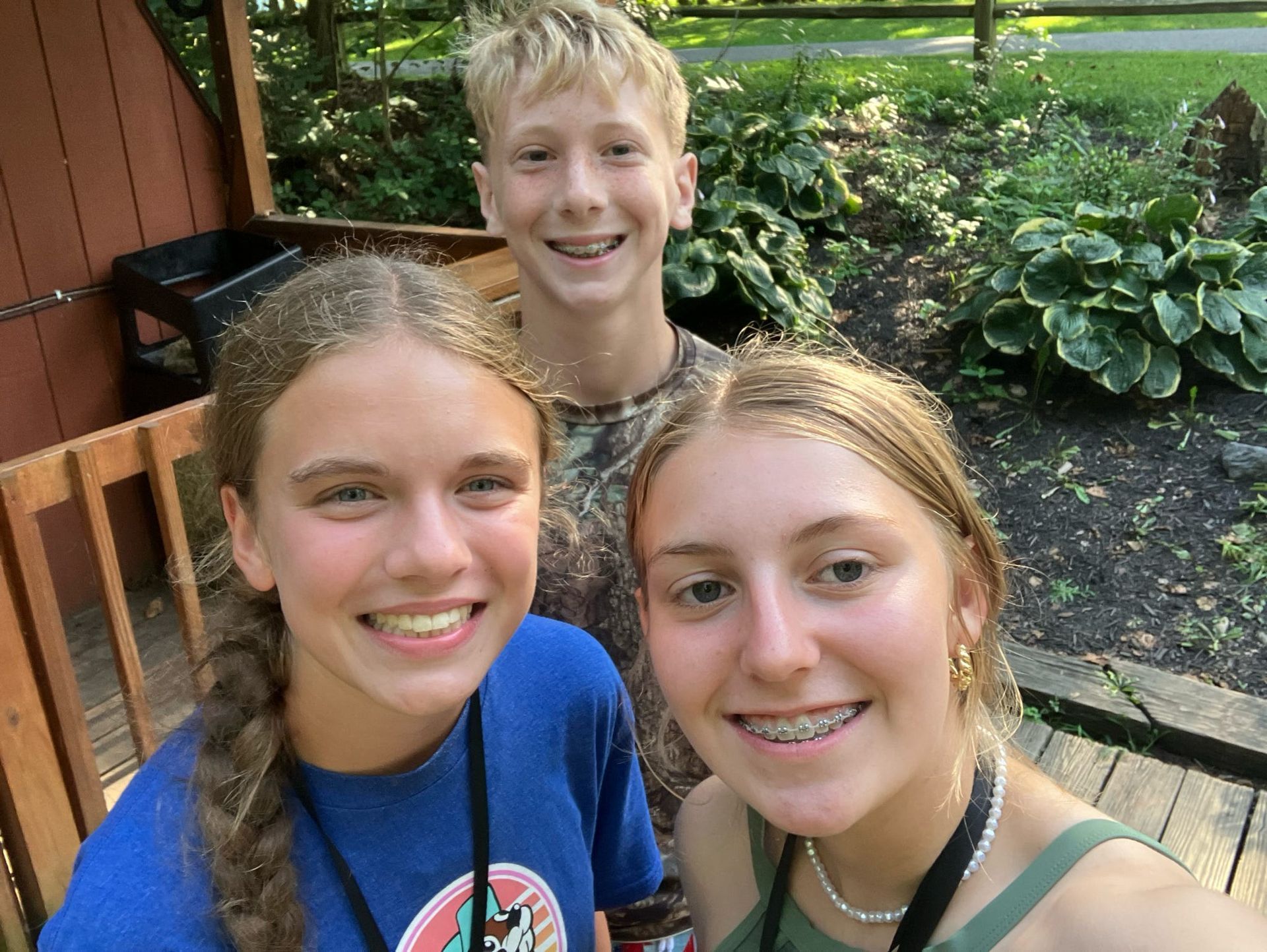Three smiling teens taking a selfie on a wooden deck in a garden.