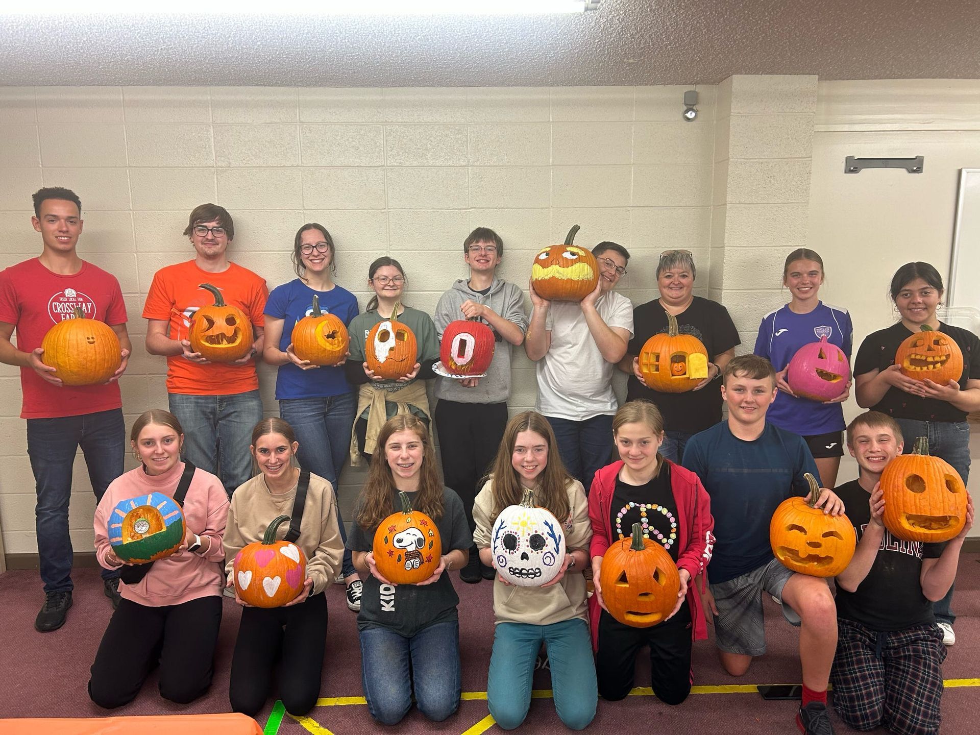 Group holding decorated pumpkins in a hallway, posing for a Halloween-themed photo.