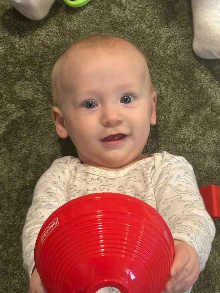 Smiling baby on carpet holding a red stacking cup