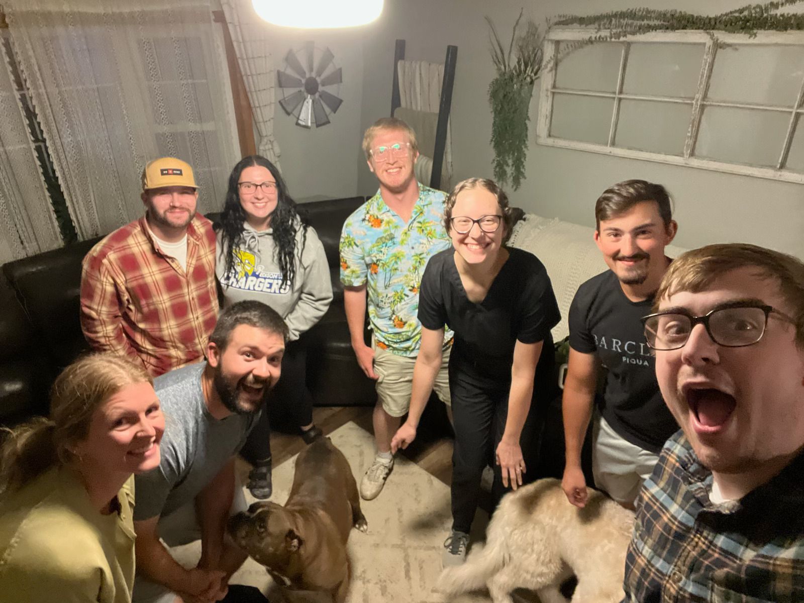 Group of people posing indoors with two dogs in a cozy, dimly lit room