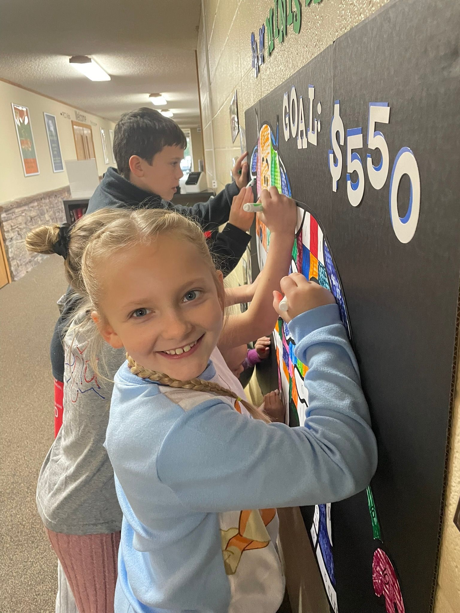 Two children decorating a classroom bulletin board with colorful number cutouts.