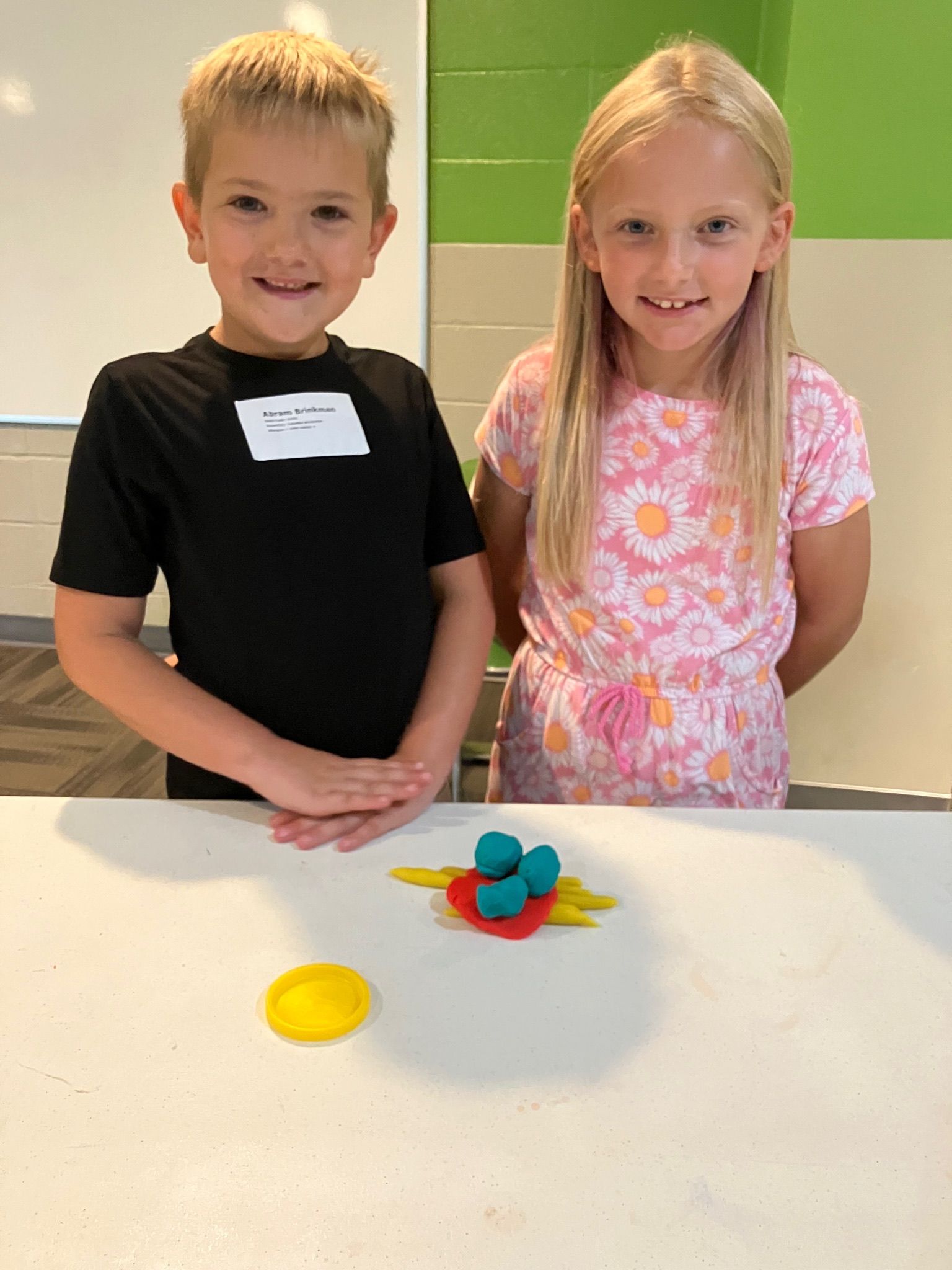 Two children standing at a table with colorful play dough shapes in front of them