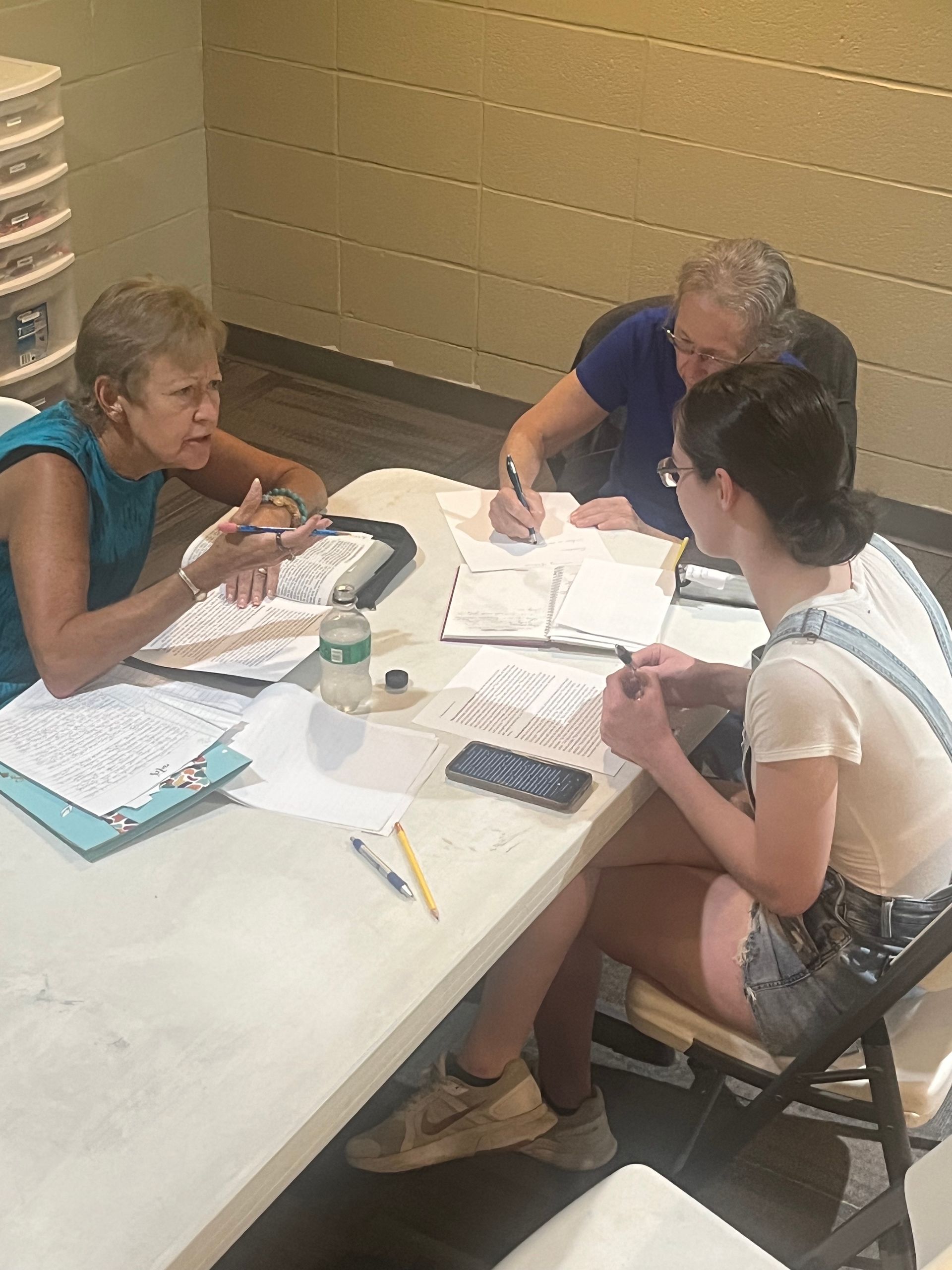 Three people sit at a table, writing on papers during a meeting.