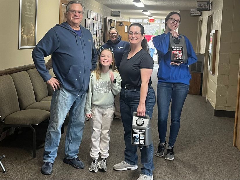 Five people standing in a hallway, smiling and holding bags and cups.