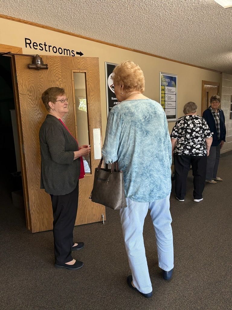 People conversing in a hallway near a restroom sign and doors.