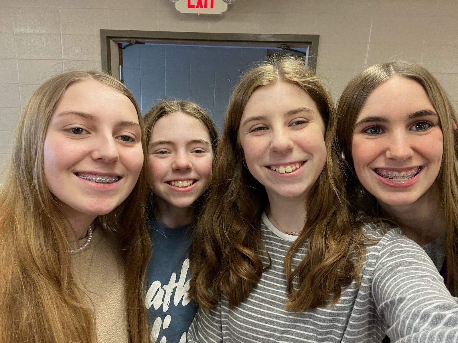 Four smiling friends pose close together indoors in front of a blue door.