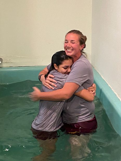 Two people hugging in a small indoor pool, both smiling and wearing wet clothes.