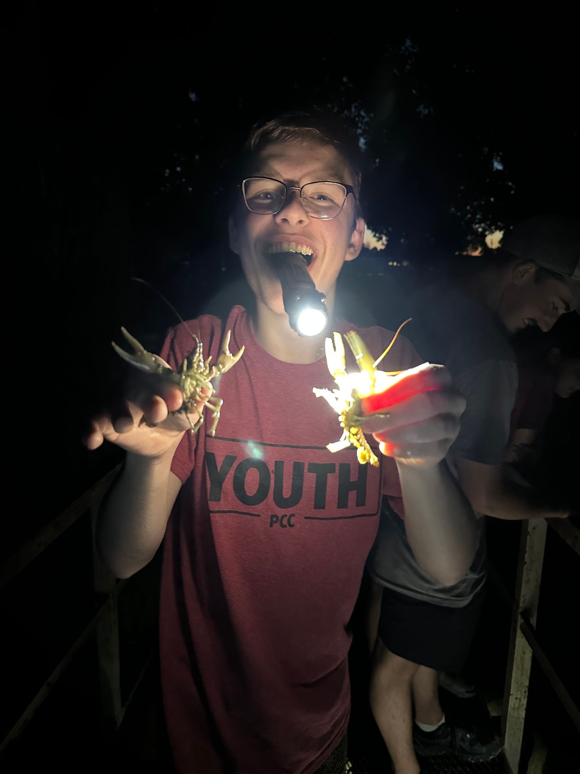 Person in a red shirt holds sparklers and a flashlight at night, smiling outdoors