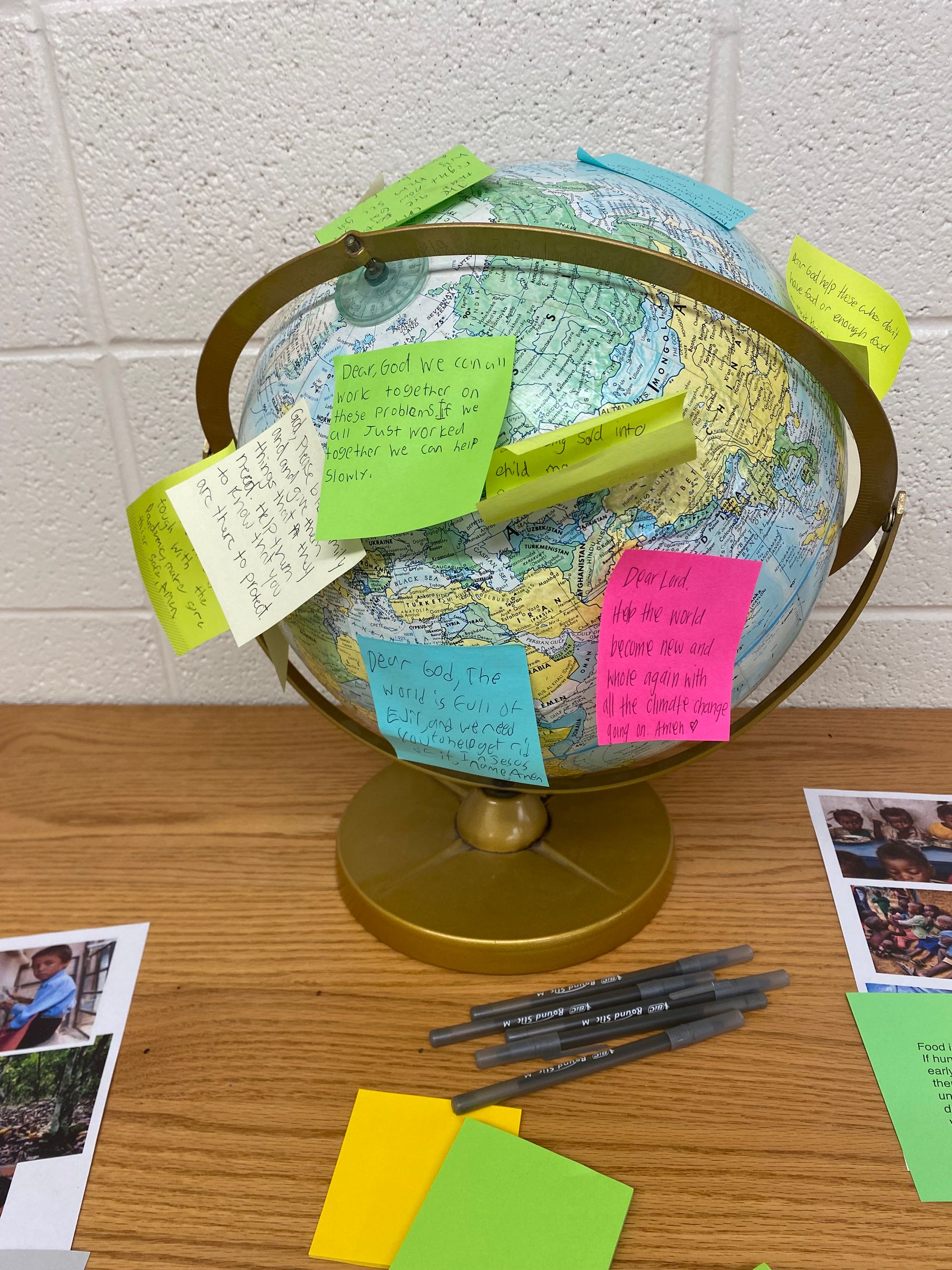 Globe display covered with colorful sticky notes on a desk against a white wall.