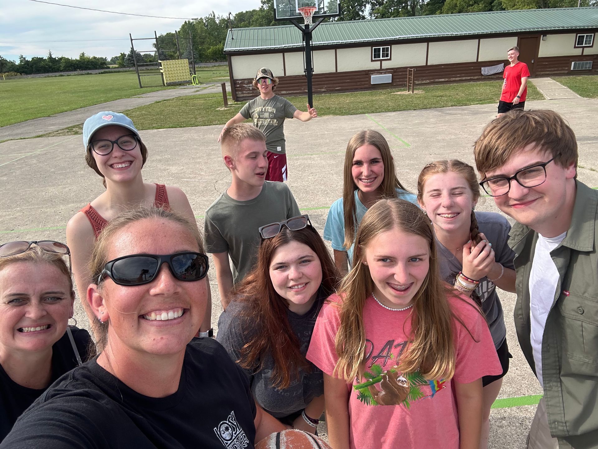 Group selfie of smiling people outdoors on a sports field, with a building in the background.