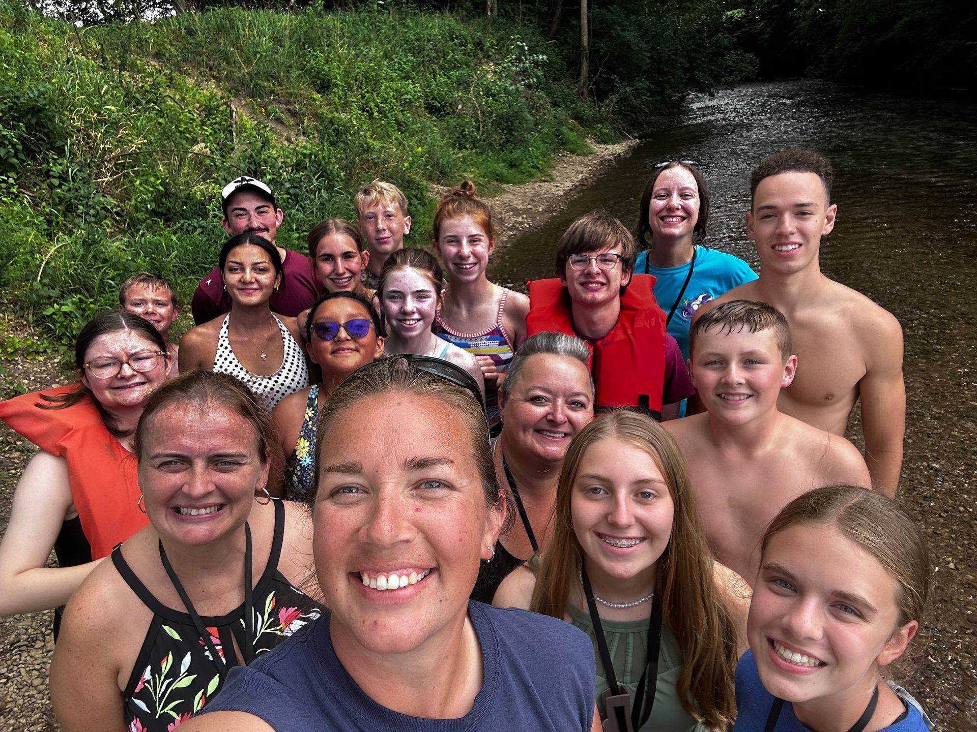 Group of smiling people in swimsuits posing closely together in a natural hot spring or pool.