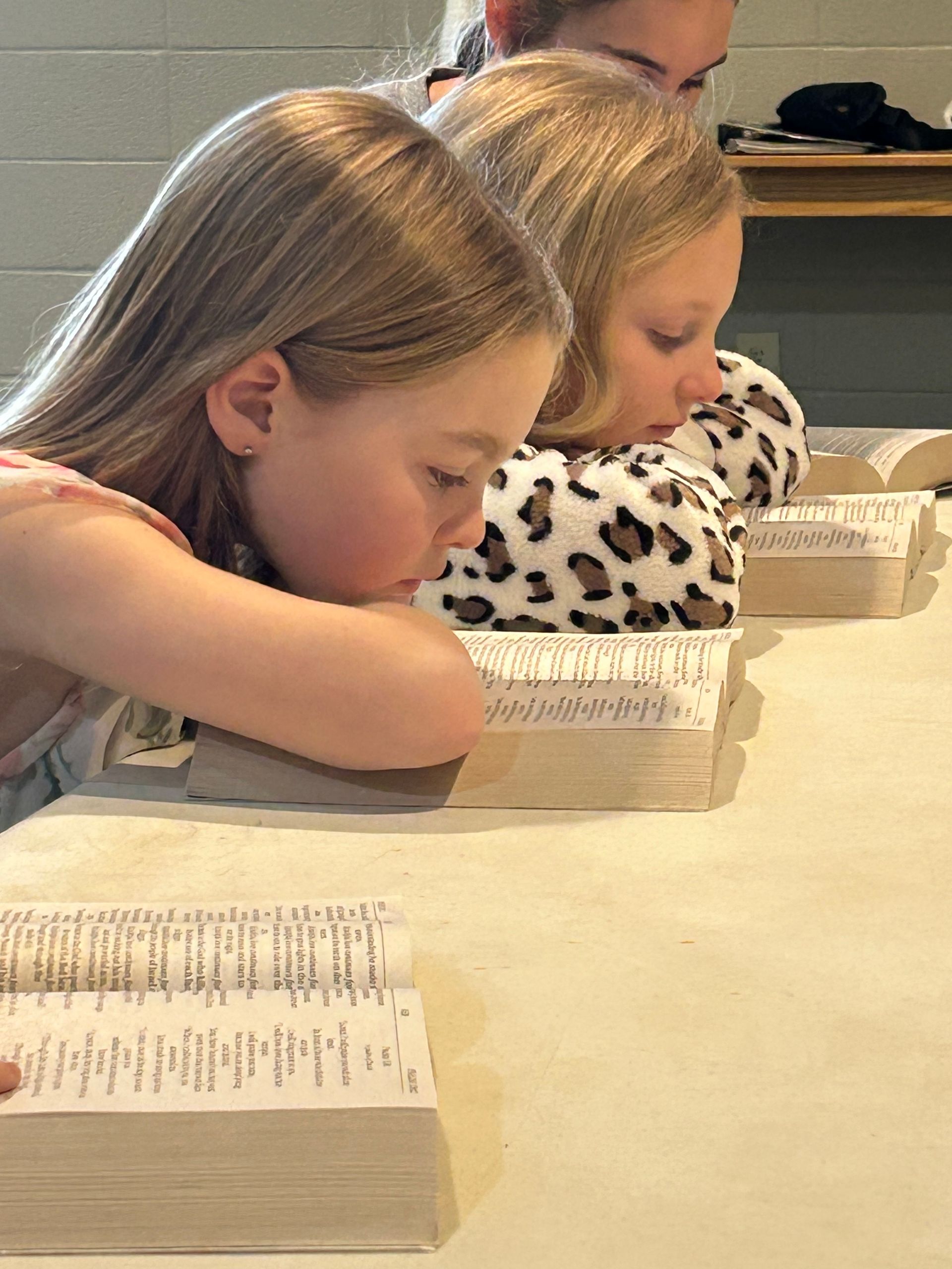Children leaning over books at a classroom table, reading quietly.