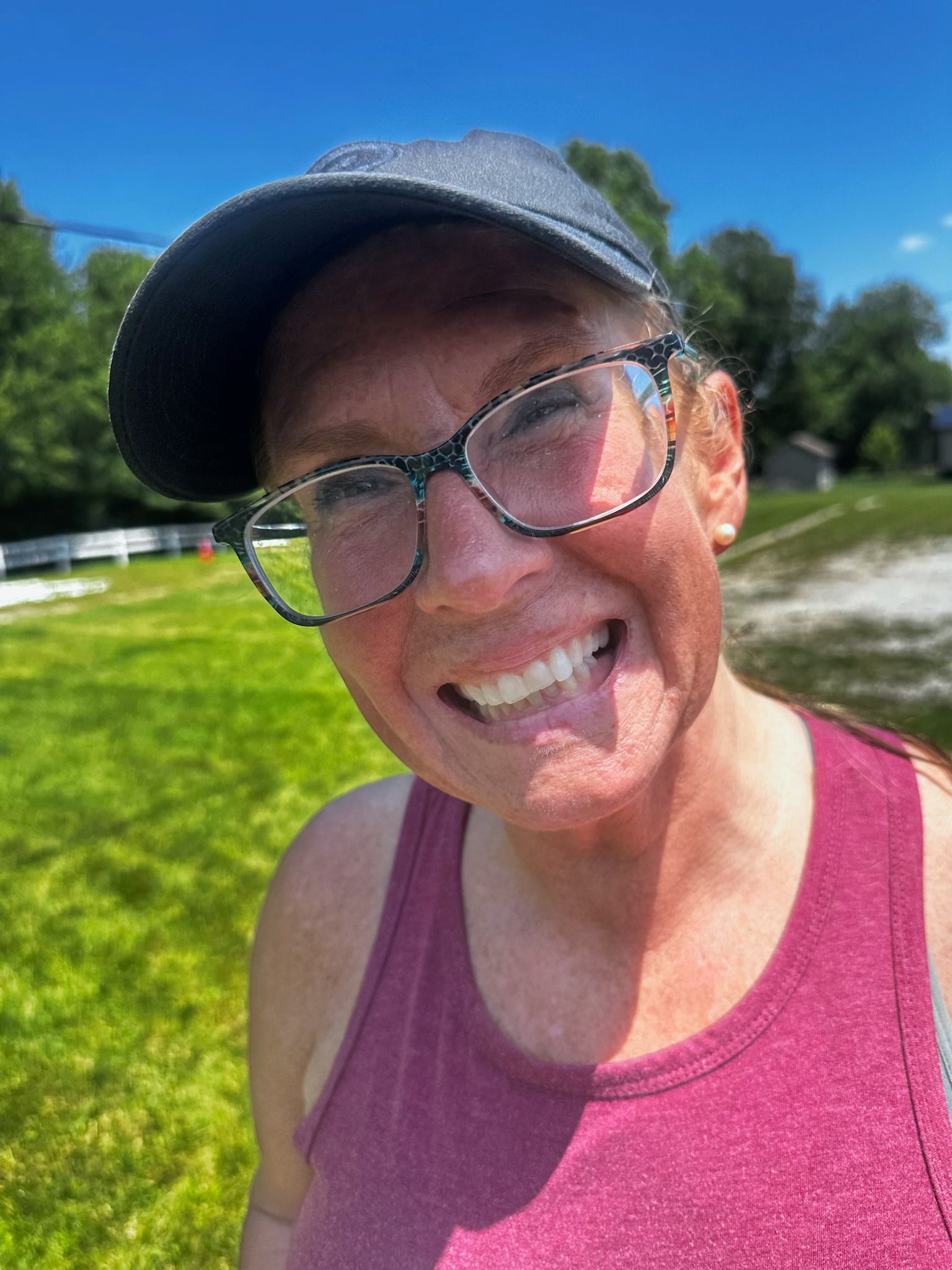Smiling person in a pink tank top and cap outdoors on a sunny grassy field