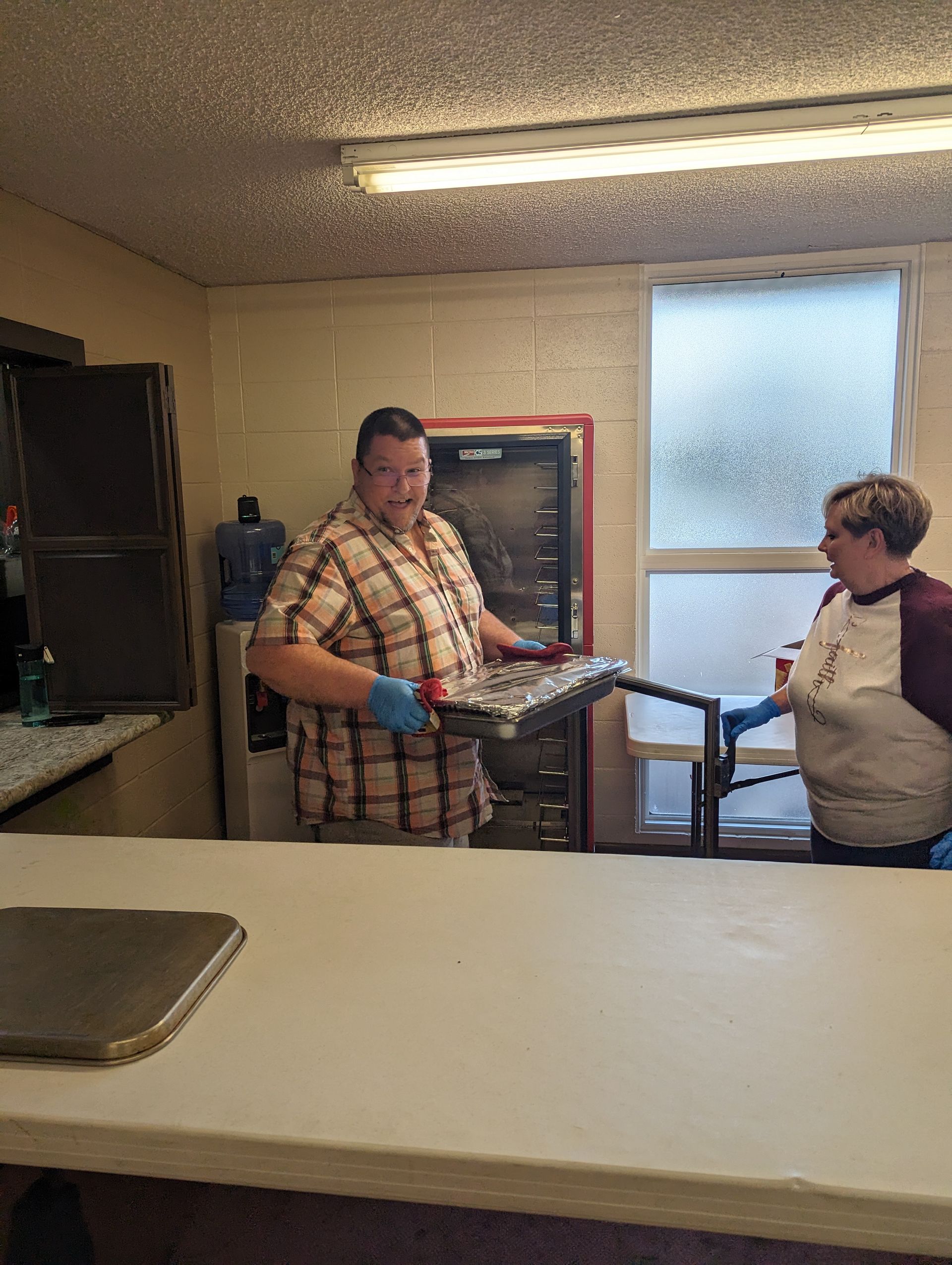 Two people in a kitchen passing a long rod, with a counter in the foreground.