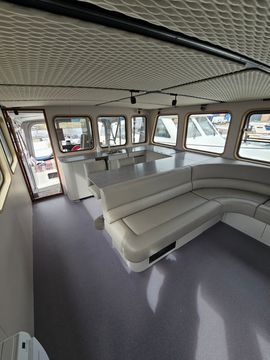 Compacte kombuis op een boot met houten kastjes, een zwart aanrechtblad, een gootsteen en ramen erboven.