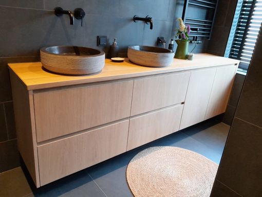 Moderne badkamer met een houten wastafelmeubel, twee waskommen, zwarte kranen en een rond vloerkleed